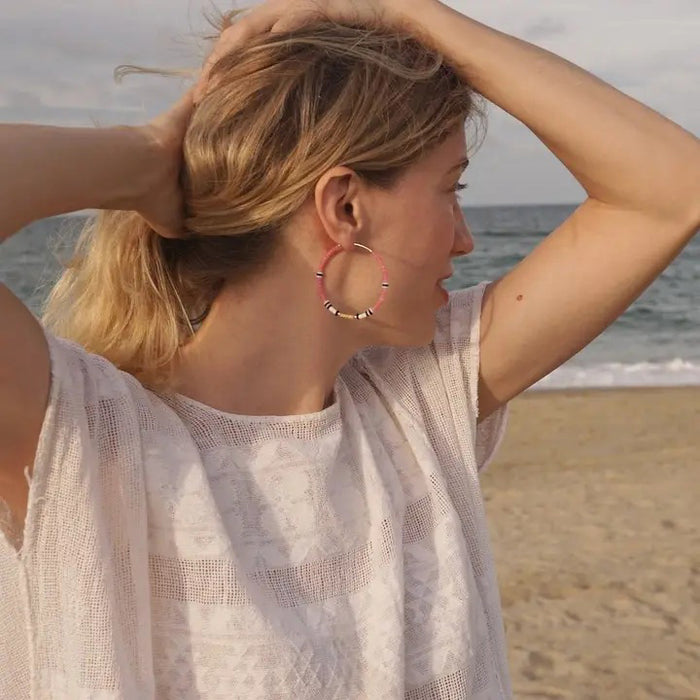 The ALICE RISE - BIG COLORLOOP EARRINGS IN SPRINGWATER by ALICE RISE feature two large hoops adorned with small, colorful Japanese glass beads, elegantly arranged and displayed on a textured light grey surface.