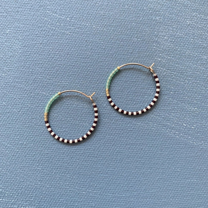 The ALICE RISE MIDI COLORLOOP EARRINGS IN SERRATA feature 14k gold filled hoops with alternating black and white beads, light blue Japanese glass beads, and gold accents—an ideal handmade jewelry piece from ALICE RISE.
