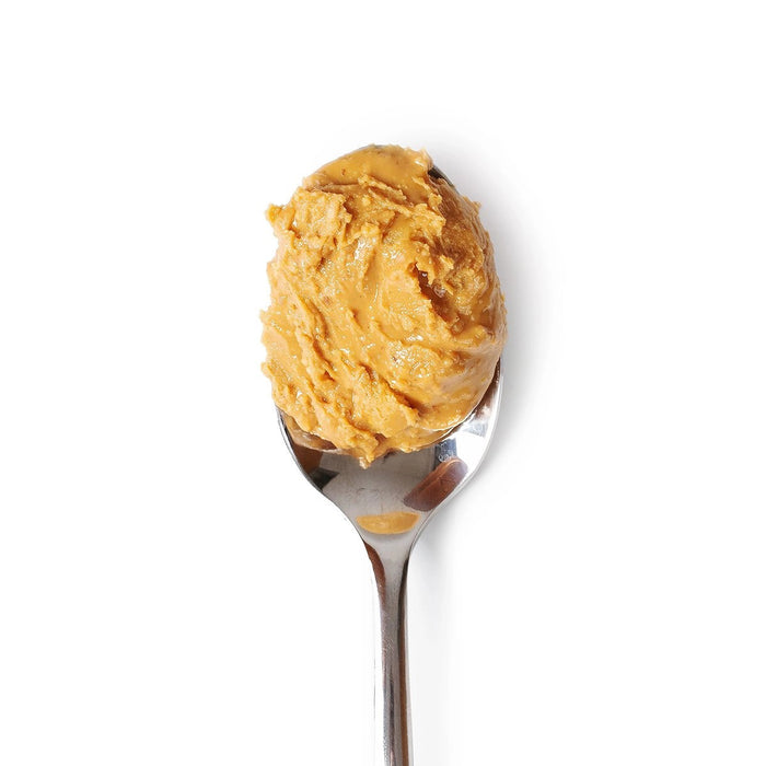 A glass jar of BIG SPOON ROASTERS - WAG BUTTER BANANA FLAX, a banana flax dog butter, with a bright yellow label and gold lid, sits on a light textured surface.
