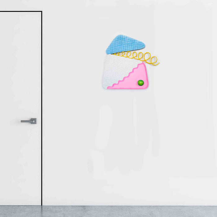 The artwork 'Loopy Cocktail Burp' features a playful three-part geometric composition with a light blue triangular top, white middle section, and pink wavy bottom segment. A yellow spiral detail and small green circular accent create visual interest. Mixed media wall sculpture utilizing wood, canvas, and acrylic paint by Ryan Patrick Martin.