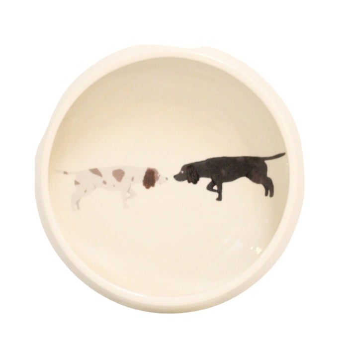 The FENELLA SMITH NEW SPANIEL DOG BOWL is a durable ceramic bowl featuring an illustration of a white dog with brown spots and a black dog touching noses inside the bottom.