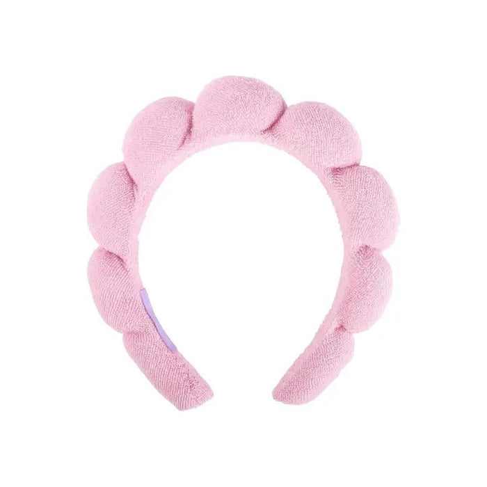 The CAIT & CO PLUSH HEADBAND is an ultra-soft, pink padded accessory featuring rounded scalloped sections like puffy petals or bubbles—ideal for elevating your skincare routine. Shown here on a white background.