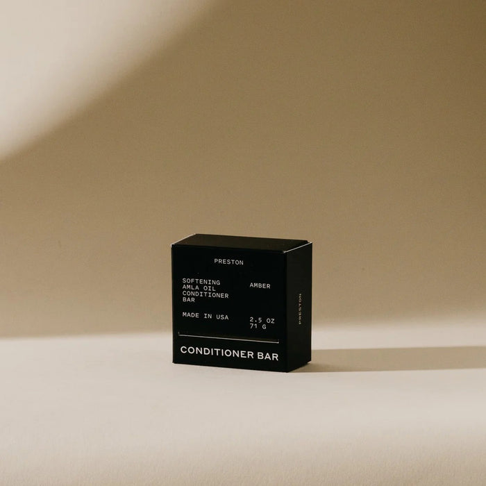 A black box labeled "PRESTON - CONDITIONER BAR" stands upright on beige, casting a shadow; the packaging notes it's softening, made in USA, plastic-free, and enriched with Indian amla oil.