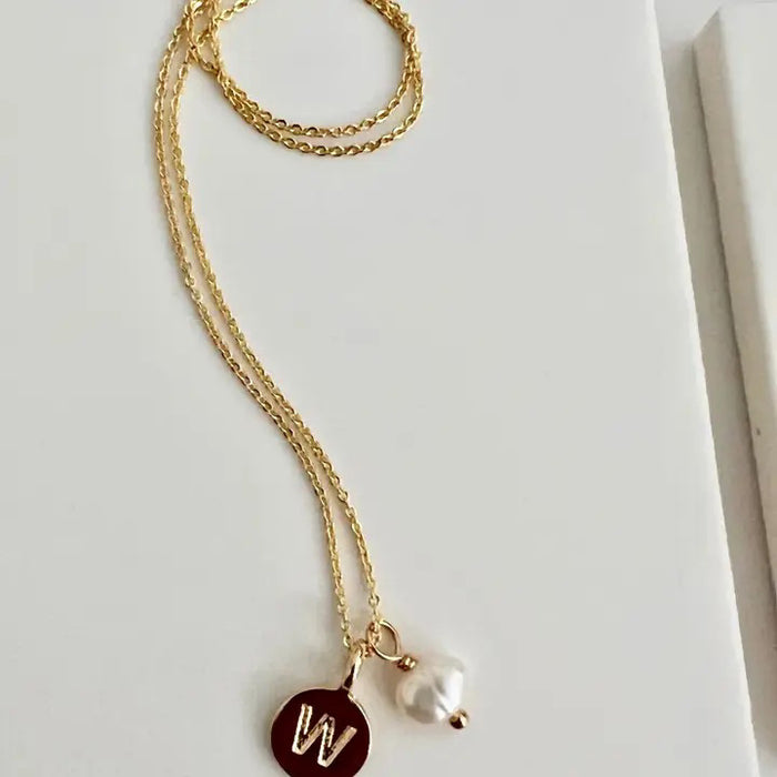 The SANDRINE FRANCE STUDIO Typwriter Initial Necklace "B" features a gold-plated round "B" pendant and a small freshwater pearl charm, handmade in NYC and shown on a white surface.