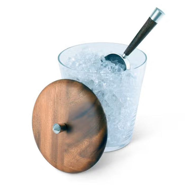 A VAGABOND HOUSE TRIBECA GLASS ICE BUCKET is displayed with an open top beside a round teak lid featuring a small handle. The Mid-Century Modern appeal of its glass and wood textures is elegantly showcased against a white background.