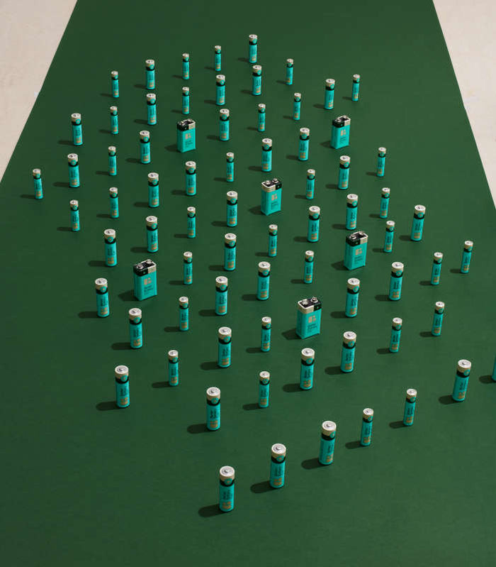 AA Alkaline Batteries by Better Battery Co are arranged on a green background to form a Christmas tree shape. The Zero Waste Batteries design incorporates both cylindrical and rectangular batteries in a symmetrical pattern.