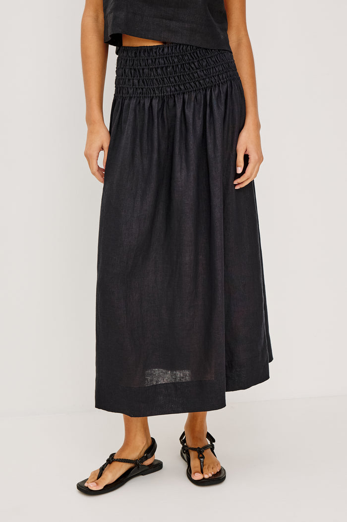 Alessa Midi Skirt in Heavy Linen With Wide Smocked Waistband and A-Line Silhouette in Black Linen Colorway - Lower Body Front View Featured on Model