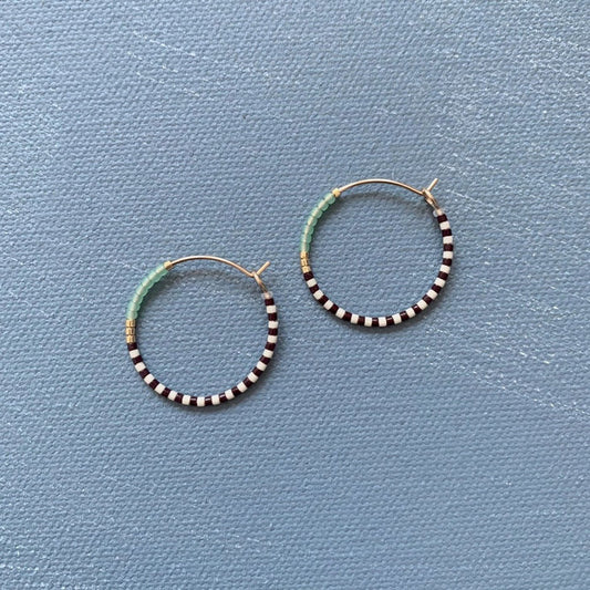 The ALICE RISE MIDI COLORLOOP EARRINGS IN SERRATA feature 14k gold filled hoops with alternating black and white beads, light blue Japanese glass beads, and gold accents—an ideal handmade jewelry piece from ALICE RISE.