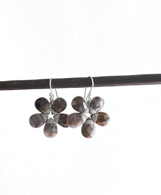 These sophisticated ANN LIGHTFOOT - Pietersite Flower Earrings showcase a graceful design with black petals complemented by sterling silver accents. Each earring is crafted with five symmetrical petals, exuding an elegant charm. Featuring convenient hooks for easy wearing, these earrings seamlessly blend style and functionality.