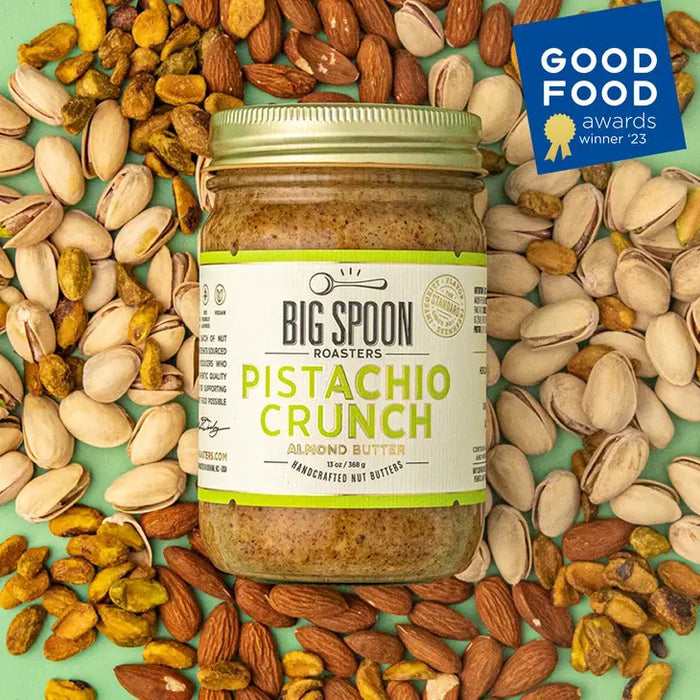 A clear glass jar of BIG SPOON ROASTERS - PISTACHIO & ALMOND CRUNCH NUT BUTTER, sealed with a gold lid and a white label with green and yellow text. The nut butter is made from heirloom mission almonds by BIG SPOON ROASTERS.