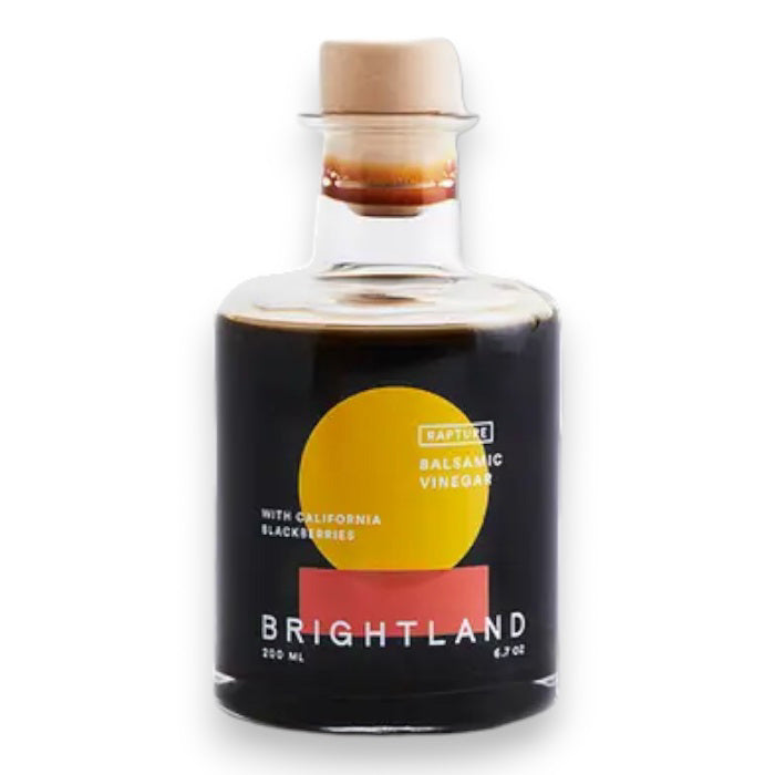 A clear glass bottle of BRIGHTLAND 'Rapture' Blackberry Balsamic Vinegar, 200 ml, featuring a red and yellow circle label stating “Balsamic Vinegar with California & triple crown blackberries.”.
