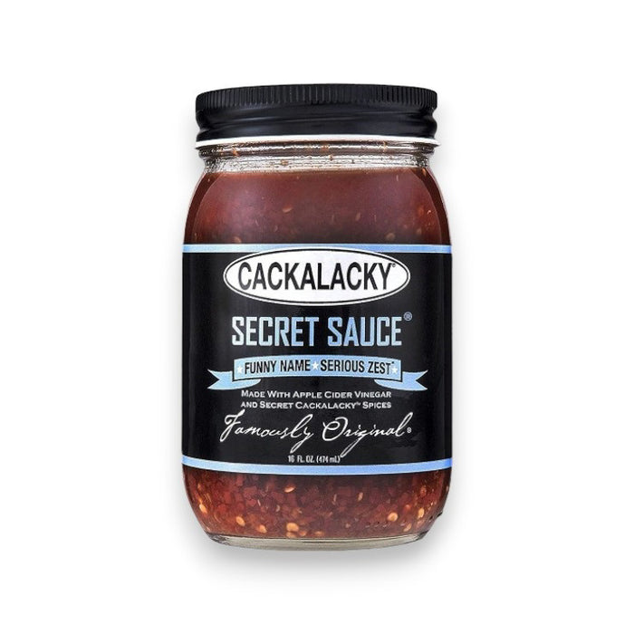 A jar of CACKALACKY - SECRET SAUCE by CACKALACKY, with a black lid and label featuring white and blue text. This Carolina vinegar sauce offers "Funny Name - Serious Zest," made with apple cider vinegar and spices, and contains rich, reddish sauce.