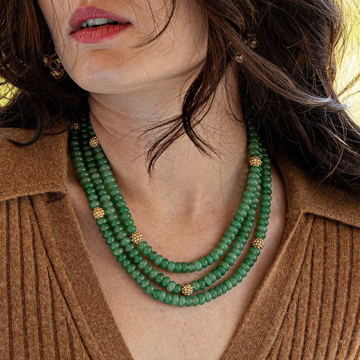 The CAPUCINE DE WULF - BERRY AND BEAD TRIPLE STRAND NECKLACE MEADOW JADE is a striking accessory with triple strands of jewel-toned jade beads, accented by small gold spheres and two large gold rings near the adjustable clasp.