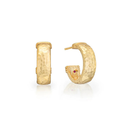 The image displays the CAPUCINE DE WULF Cleopatra Classic Small Hoop Earrings, showcasing artisan craftsmanship. Both gold hoops have hammered finishes, open-back designs, and subtle indentations. One earring includes a small red gem near the clasp, all set against a white background.