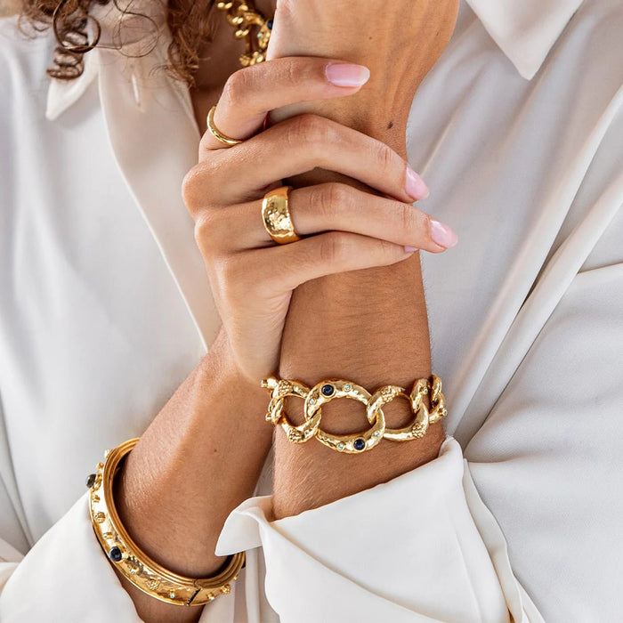 The CAPUCINE DE WULF CLEOPATRA RING SIZE 8, crafted in polished gold with a hammered texture, sits elegantly on a plain white background, highlighting the allure of handmade jewelry.
