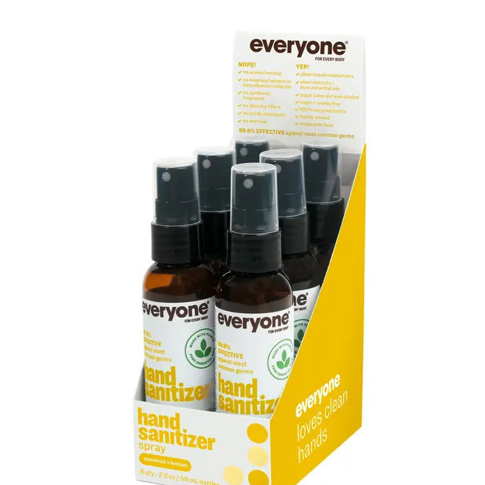 A 2 oz bottle of EVERYONE FOR EVERYBODY Coconut & Lemon Hand Sanitizer Spray is partially visible inside an open brown leather bag, beside black sunglasses and a dark wallet on a light surface.