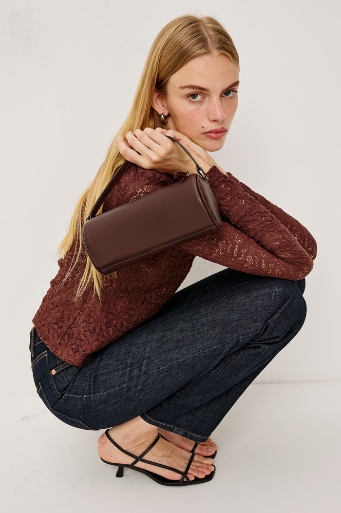 Como Mini Barrel Bag in Italian Leather With Fixed Top Strap, Removable and Adjustable Buckled Crossbody Strap, Top Zipper, Side-Embossed Logo, Branded Interior Label in Espresso Colorway - Stylized Model Featured