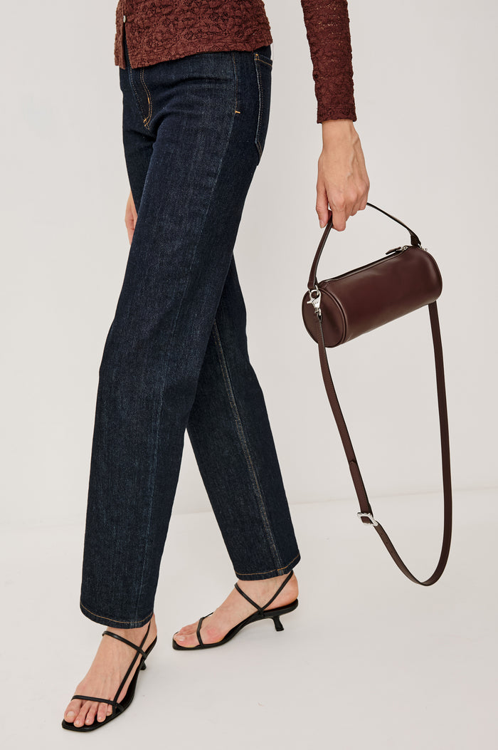Como Mini Barrel Bag in Italian Leather With Fixed Top Strap, Removable and Adjustable Buckled Crossbody Strap, Top Zipper, Side-Embossed Logo, Branded Interior Label in Espresso Colorway - Stylized Model Featured