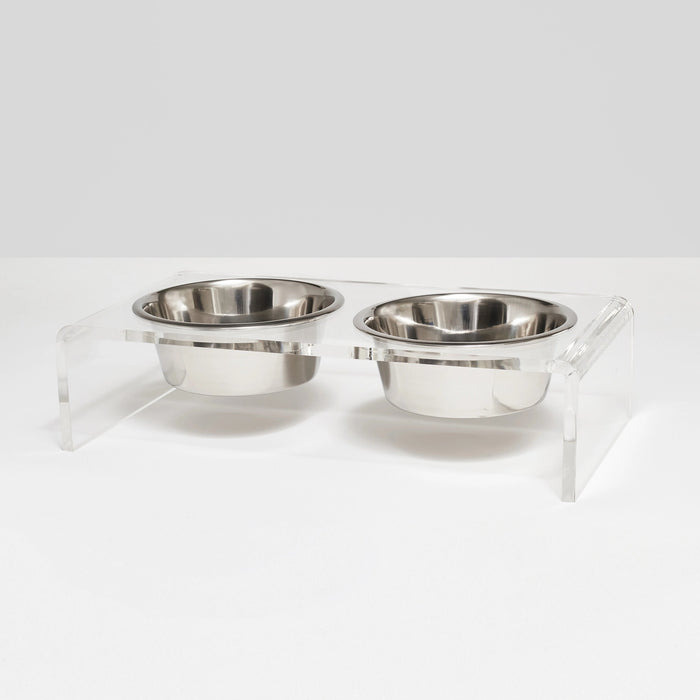 The HIDDEN ELEVATED PET FEEDER 1 QUART (CLEAR) features two stainless steel bowls set side by side in a clear acrylic base, creating a stylish and modern raised double bowl feeder.