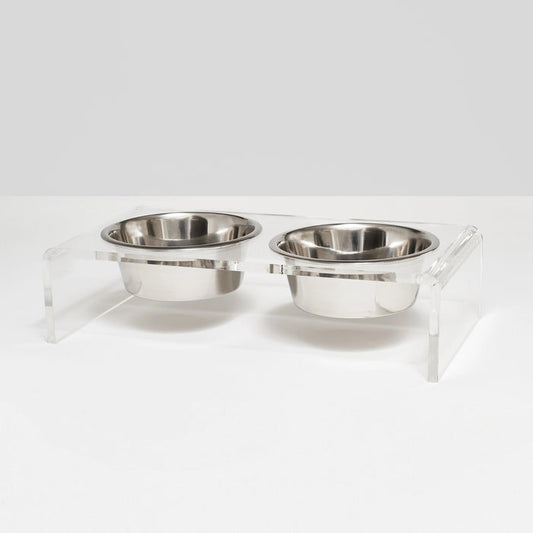 The HIDDEN ELEVATED PET FEEDER 1 QUART (CLEAR) features two stainless steel bowls set side by side in a clear acrylic base, creating a stylish and modern raised double bowl feeder.