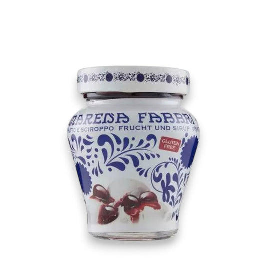 A white and blue ceramic jar featuring intricate floral and geometric patterns, labeled "FABBRI - AMARENA CHERRIES IN SYRUP" in blue text under the brand name "GOURMET FOOD SOLUTIONS." The jar contains Italian tart cherries in syrup, promising a delightful sour taste and displaying a red "Gluten Free" label. The jar is photographed against a light gray background.