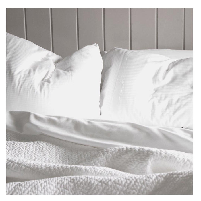 The FEARRINGTON HOUSE FEARRINGTON LIFESTYLE BEDDING COLLECTION - QUEEN LINEN EXPERIENCE features two white pillows, a crisp sheet set, and a textured blanket on a paneled wall, illuminated by soft natural light for an inviting, luxurious look.