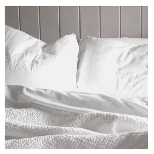 The FEARRINGTON HOUSE FEARRINGTON LIFESTYLE BEDDING COLLECTION - QUEEN LINEN EXPERIENCE features two white pillows, a crisp sheet set, and a textured blanket on a paneled wall, illuminated by soft natural light for an inviting, luxurious look.