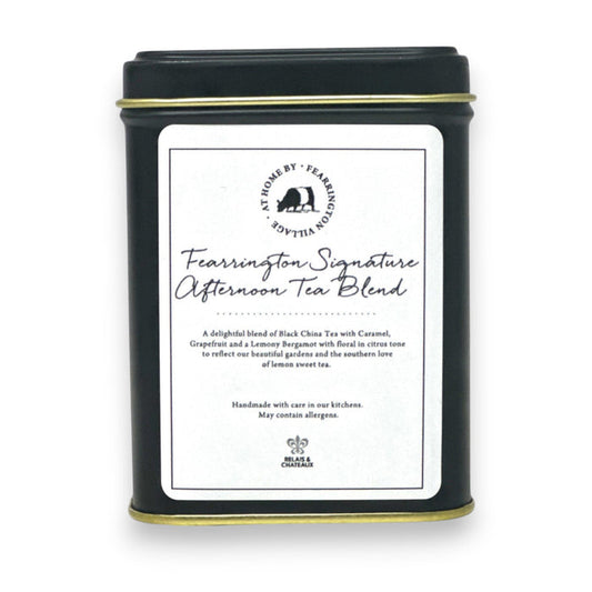 A black tin labeled "Fearrington Signature Afternoon Tea Tin" from the Fearrington House Signature Collection contains a luxurious blend of Loose Leaf Black China Tea with caramel, grapefruit, and lavender. The tin has a simple, elegant design accented by a white label featuring the product description.