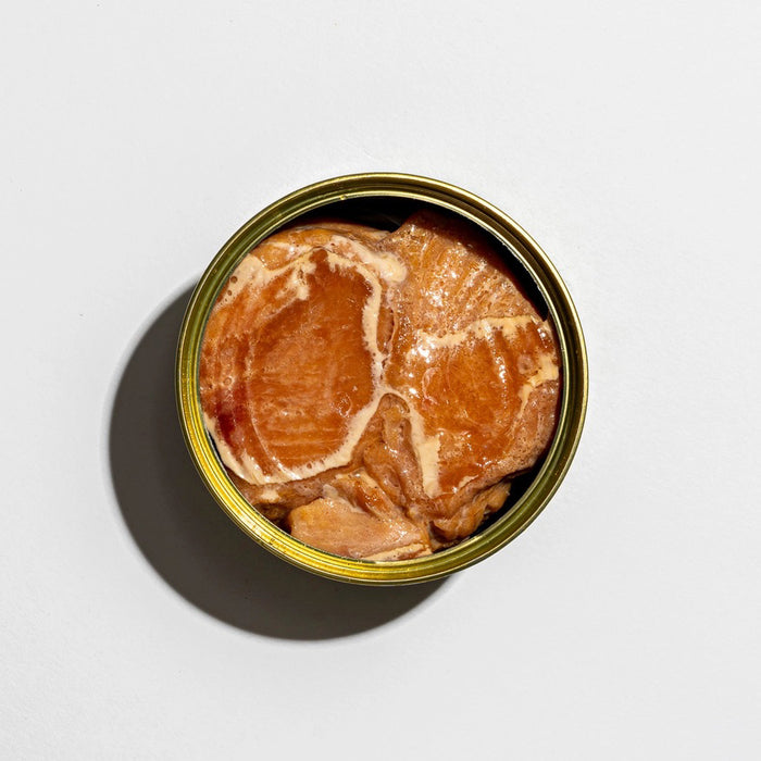 An open can of FISHWIFE - WILD CAUGHT SPICY ALBACORE TUNA, showing large, light brown pieces packed in oil or sauce, against a plain white background.