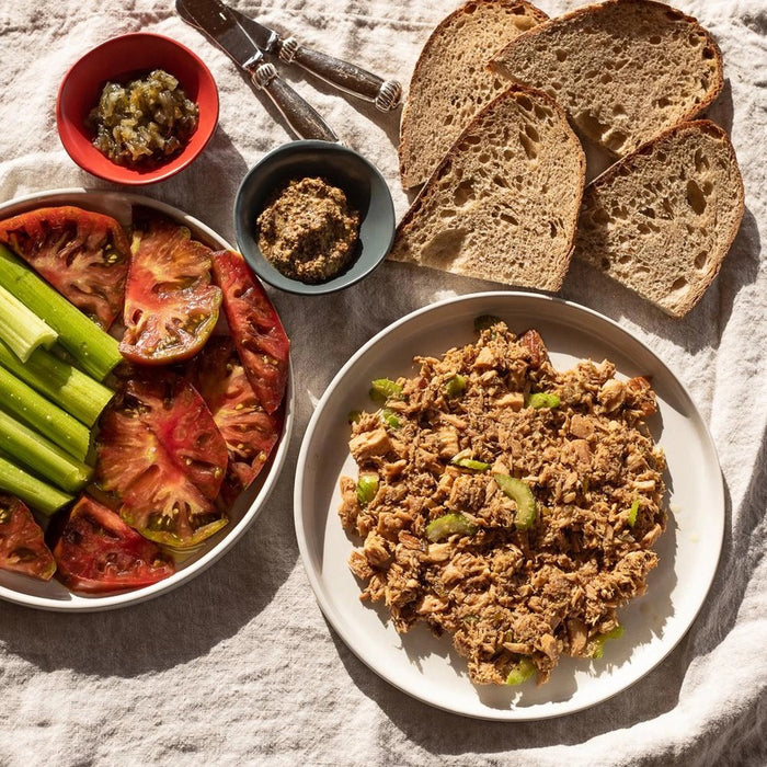 An open can of FISHWIFE - WILD CAUGHT SPICY ALBACORE TUNA, showing large, light brown pieces packed in oil or sauce, against a plain white background.