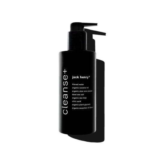 A sleek black pump bottle labeled "JACK HENRY - CLEANSE+ FACE" features hydrating botanicals and natural ingredients. Photographed on a white background with a bold shadow, this all-in-one cleanser combines purity and simplicity.