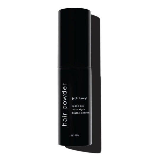 A shirtless person holds a black JACK HENRY – HAIR POWDER bottle, a dry shampoo with smectite, micro algae for growth and shine, and arrowroot to absorb oil—leaving hair clean and matte.