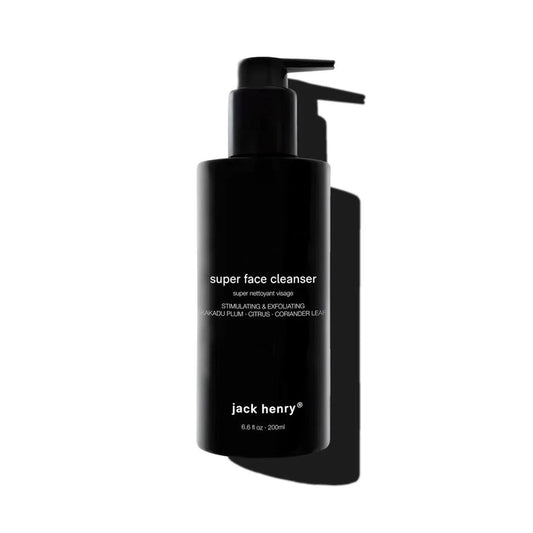 A person with short curly hair gently massages JACK HENRY - SUPER FACE CLEANSER onto their face, while ingredient callouts highlight bamboo powder for exfoliation, kakadu plum for brightening, and willow bark for cell renewal.