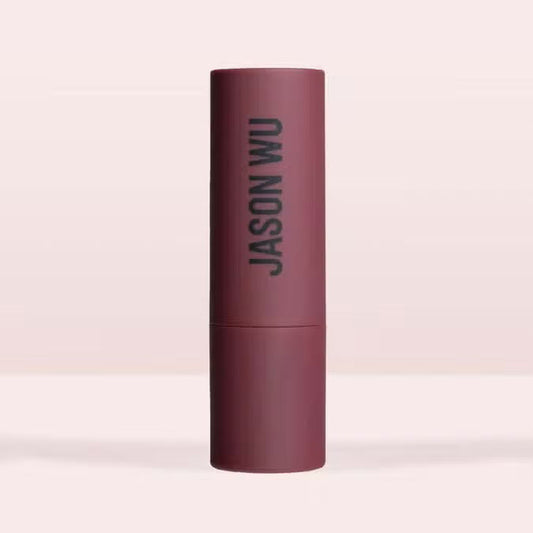 A burgundy JASON WU BEAUTY HOT FLUFF LIP/EYE/CHEEK matte lipstick stands upright with the brand name printed vertically, set against a pale pink background.