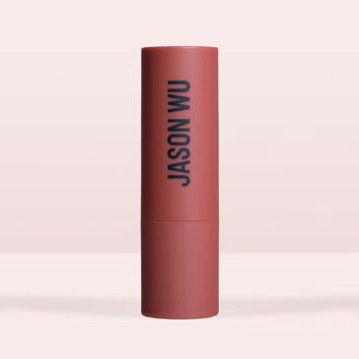 A burgundy JASON WU BEAUTY HOT FLUFF LIP/EYE/CHEEK matte lipstick stands upright with the brand name printed vertically, set against a pale pink background.