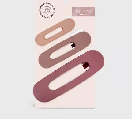 A pink card presents the KITSCH - FLAT LAY CLAW CLIP 3 PCS, featuring three clips in gradient shades of pink and mauve, from light to dark. Adorned with a logo and text, it emphasizes their crafting from recycled plastic.
