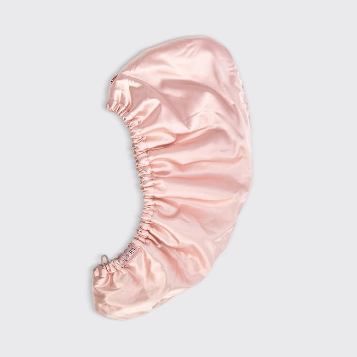 The image displays a beige box with the KITSCH Satin Wrapped Hair Towel inside. The packaging shows an illustration of the towel and a smiling person wearing it, emphasizing its benefits for reducing frizz in damaged, curly, or frizzy hair.