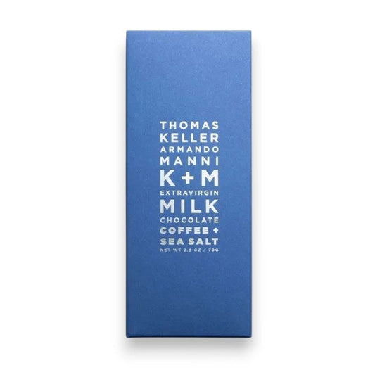 A blue package of K & M EXTRAVIRGIN CHOCOLATE, labeled “K+M - EXTRAVIRGIN MILK CHOCOLATE, COFFEE AND SEA SALT BAR” in centered white text, featuring a rich blend of roasted coffee bean and sea salt flavors.