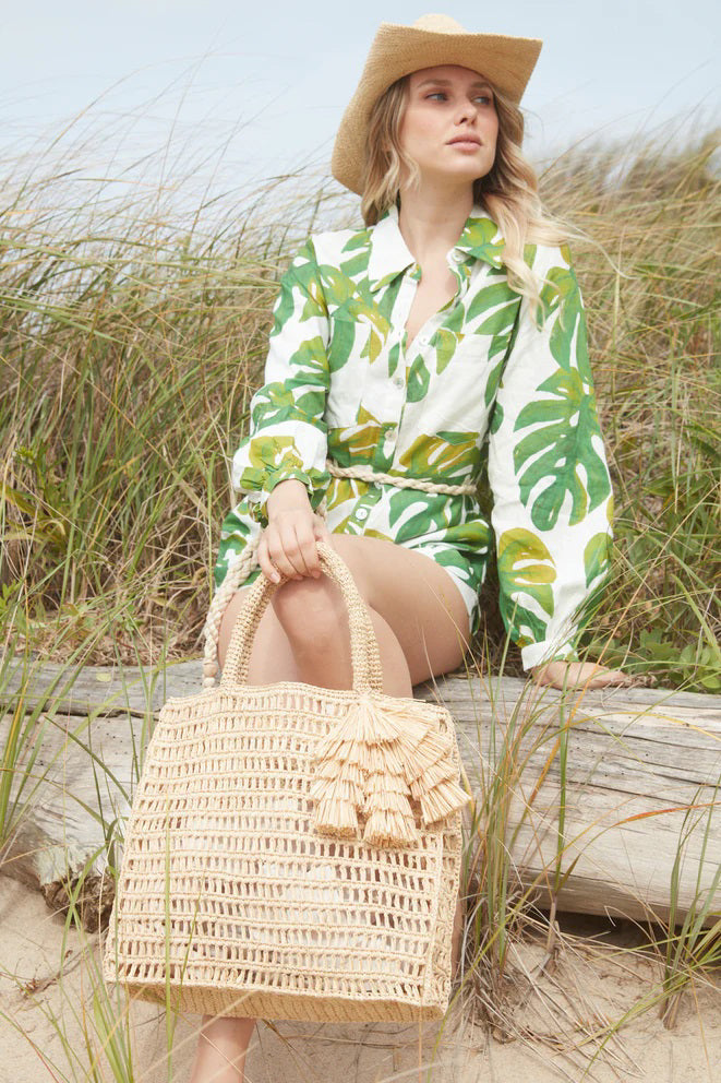 The MAR Y SOL - GEORGIA TOTE by MAR Y SOL is a rectangular crocheted raffia bag with two handles and a decorative tassel, shown against a white background.