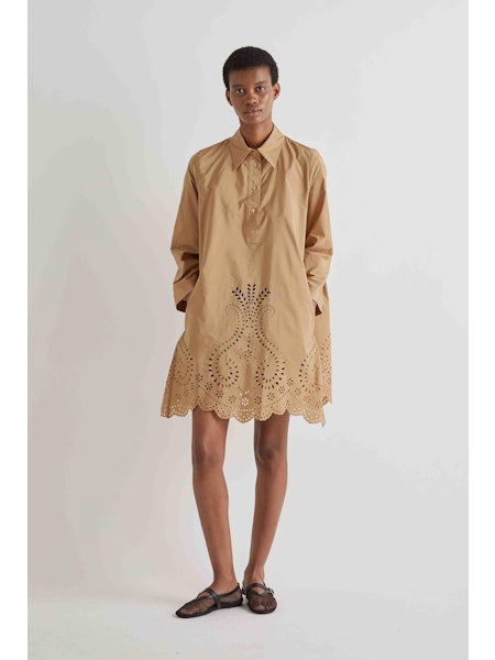 A person stands against a white background wearing the MEIMEIJ Lasercut Cotton Shirt Dress featuring eyelet embroidery and scalloped cuff hems, paired with black flat shoes.