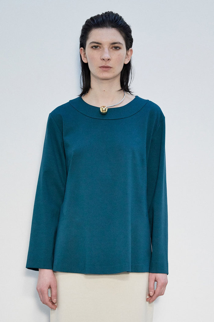 A woman with straight dark hair wears the MEIMEIJ Long Sleeve Ponte Swing Top in teal and a gold pendant necklace, standing against a plain light background, facing forward with a neutral expression.