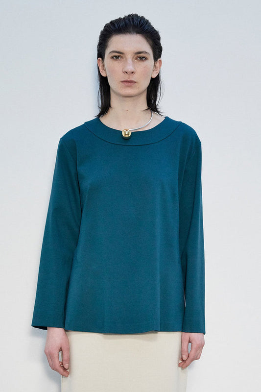 A woman with straight dark hair wears the MEIMEIJ Long Sleeve Ponte Swing Top in teal and a gold pendant necklace, standing against a plain light background, facing forward with a neutral expression.