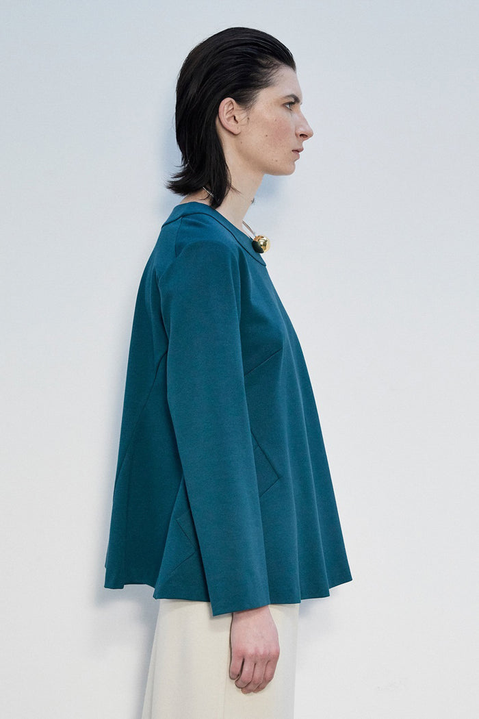 A woman with straight dark hair wears the MEIMEIJ Long Sleeve Ponte Swing Top in teal and a gold pendant necklace, standing against a plain light background, facing forward with a neutral expression.
