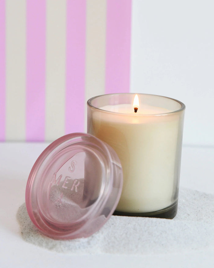 The MERSEA Coconut Sugar Jolie Jar Candle features a beige soy wax blend in a clear glass jar with a light pink lid, shown against a white background.