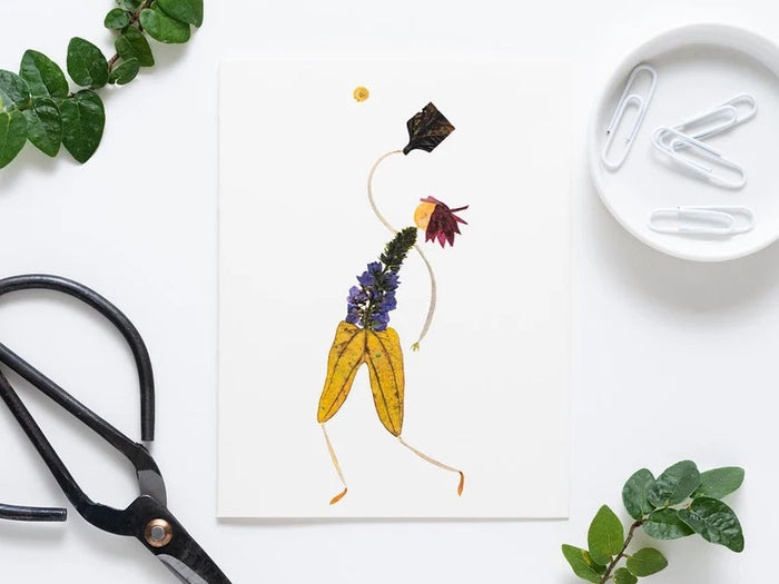 The PETAL PEOPLE PRESS - PICKLEBALL GREETING CARD by Petal People Press features a whimsical figure made of pressed flowers and leaves on a white background, posed dynamically with a black leaf racket and yellow flower ball, resembling an elegant pickleball moment.