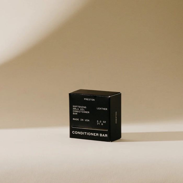 A black box labeled "PRESTON - CONDITIONER BAR" stands upright on beige, casting a shadow; the packaging notes it's softening, made in USA, plastic-free, and enriched with Indian amla oil.