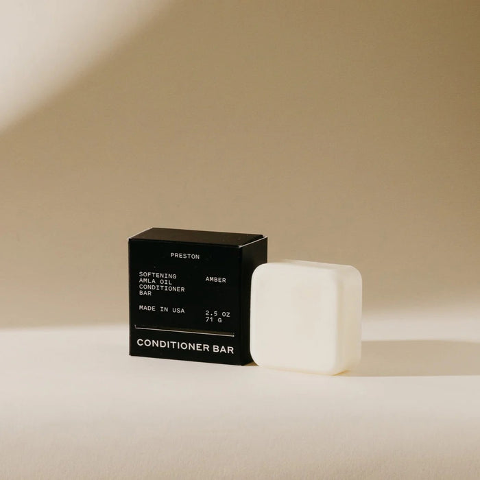 A black box labeled "PRESTON - CONDITIONER BAR" stands upright on beige, casting a shadow; the packaging notes it's softening, made in USA, plastic-free, and enriched with Indian amla oil.