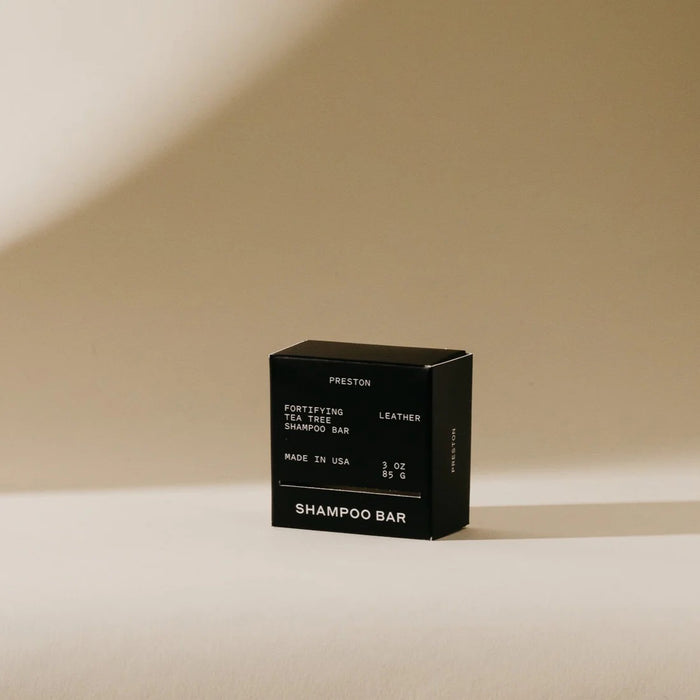 A black box labeled “PRESTON - SHAMPOO BAR” from the brand PRESTON rests on a beige surface with soft shadows. This 3 oz sulfate-free, USA-made bar offers an eco-friendly, plastic-free shampoo solution.