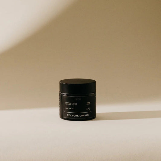 A black PRESTON - TEXTURED LOTION jar rests on a light surface, its shadow softly cast against a beige backdrop—ideal for anyone wanting a matte finish and light hold from the trusted PRESTON brand.