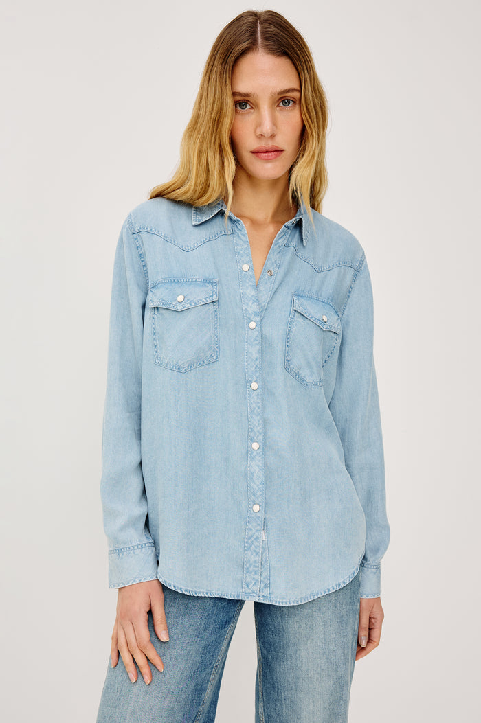Remi is a utility-style Tencel denim shirt with a relaxed fit. The shirt features a notched collar, two front flap pockets, and faux horn buttons etched with a logo in medium indigo colorway - Front View Featured on Model